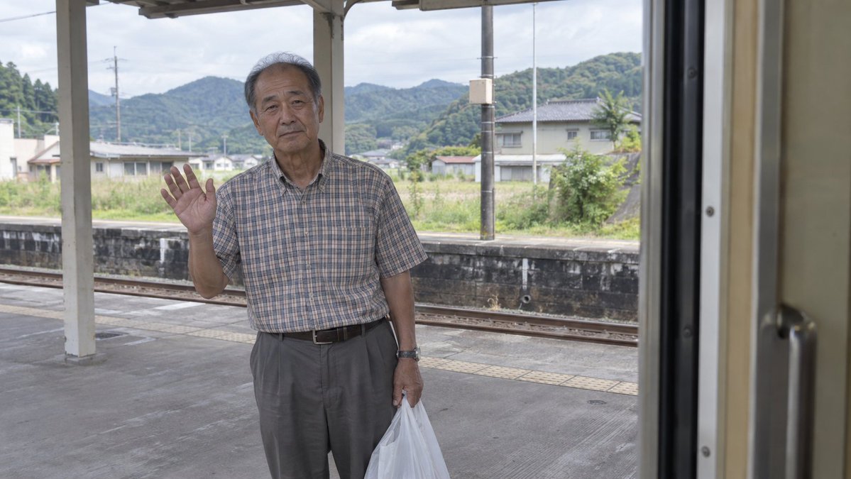 Elderly Man Waving at Rural Station — example output